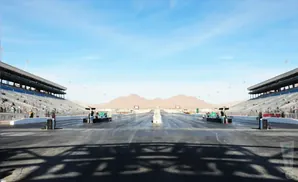 A drag strip with bleachers, mountains, and clear blue sky.