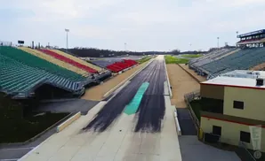 Aerial view of a drag strip with colorful stadium seating and a building.