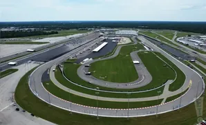 Aerial view of a large oval-shaped racetrack with grandstands, green infields, and surrounding roads and parking areas.