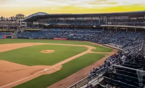 A baseball stadium with seats filled with spectators during a sunset game.