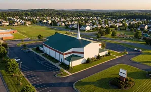 Aerial view of a white church with a green roof and steeple, surrounded by a suburban neighborhood.