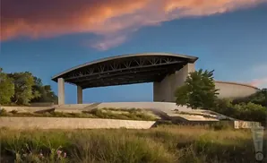 An outdoor amphitheater with a curved roof stands against a blue sky with orange clouds.
