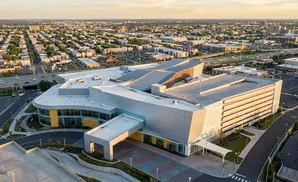 Aerial view of a modern complex with a large, multi-story building and surrounding urban landscape at sunset.