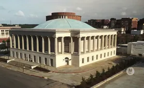 An aerial view of a building with a large dome and classical columns, framed by a street and surrounding structures.