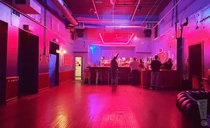 Interior of a bar with neon lights, a bar, and people.