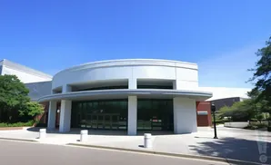 Modern curved building entrance with glass doors and white pillars, under a clear blue sky.