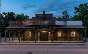 Rustic wooden building with a covered porch and twin doors, resembling an old Western storefront.