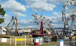 A carnival with rides like a Ferris wheel and a spinning pendulum ride under a cloudy blue sky.