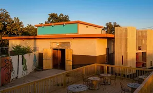 A building with a bright teal sign, orange trim, and a wooden deck with tables and chairs.