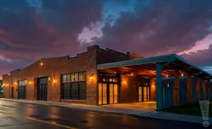 Exterior of a brick building with large windows and a covered entryway at dusk.