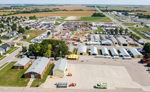 Aerial view of a fairgrounds with rides, games, buildings, and surrounding residential and agricultural areas.