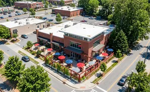 An aerial view of a brick building with an outdoor patio filled with tables and umbrellas.