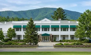 A white building with green awnings sits before a mountain.