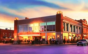 A vibrant sunset casts a warm glow on a bustling street with people dining outdoors and a car driving by.