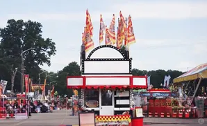 A lively street fair with a prominent food stall adorned with flags and bright lights.