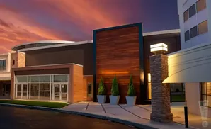 Modern building at dusk with warm wood accents, stone pillar, and a vibrant sunset sky.
