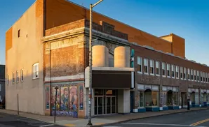 Exterior of a historic brick theater with a marquee, large mural, and arched storefront windows.