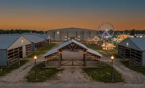 Aerial view of a fairground at dusk, featuring barns, a wooden archway, and carnival rides like a Ferris wheel.