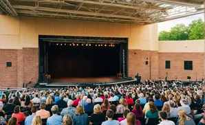 An outdoor amphitheater crowd faces a stage under a large roof.