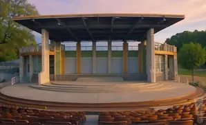 An outdoor amphitheater stage with seating in the foreground under a pink sky.