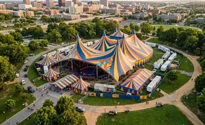 Aerial view of a circus tent with colorful stripes, surrounded by trees and buildings.