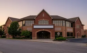 A brick office building with large windows and a blank sign above arched double doors at sunset.