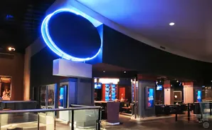 A large blue neon ring hangs above a bar area in a modern building.