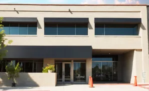 A modern tan brick building with dark awnings over windows and doors.