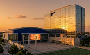Modern glass office building and arena lit by sunset, with a large outdoor screen.