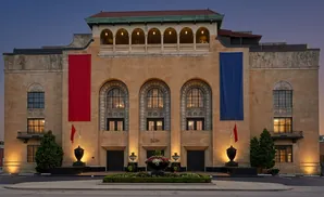 Grand stone building with red and blue banners, arched windows, and urns at dusk.