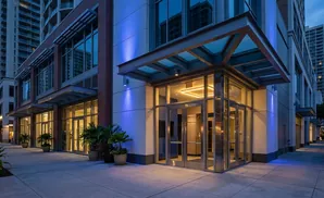 Modern building entrance at dusk with glass doors, illuminated by blue and warm interior lights.