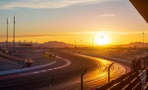 Sunset over a race track with mountains in the distance and stadium seating on the left.