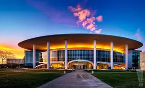 A modern circular building with glass walls and a wide overhang at sunset.