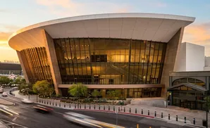 A modern, curved building with glass windows and stone accents at sunset, with cars blurred by motion on the street.