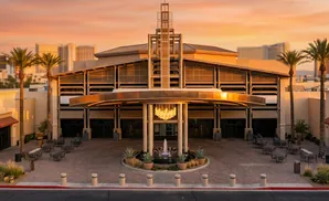 Exterior view of a large building entrance with palm trees and a fountain at sunset.