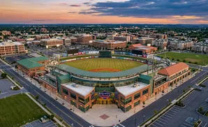Aerial view of a baseball stadium with surrounding buildings and cityscape at sunset.