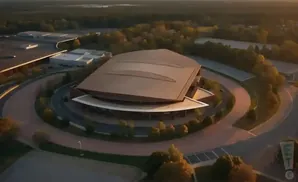 Aerial view of a large, modern building with a curved, metallic roof, surrounded by trees and a circular driveway.