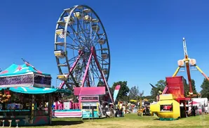 A carnival scene with a Ferris wheel, rides, and game booths under a clear blue sky.