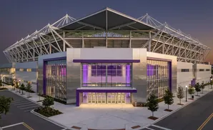 A modern stadium at dusk with purple lighting and a silver exterior.