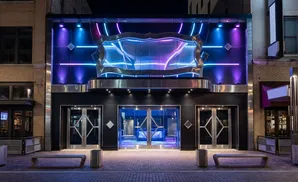 Exterior of a modern building at night, featuring colorful neon lights, glass doors, and benches.