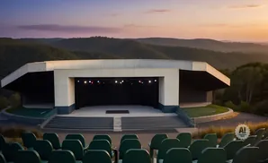 Outdoor amphitheater stage with hills and sunset in background, with empty seats in foreground.