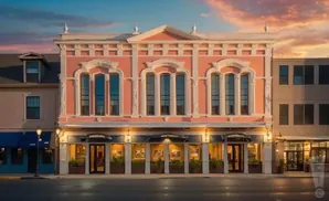 A pink historic building with ornate details stands on a street at sunset.