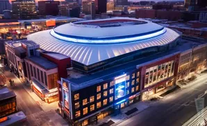 Aerial view of an illuminated domed stadium with surrounding buildings at dusk.