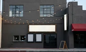 Exterior of a dark gray building with a marquee, string lights, and a red awning.