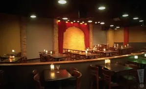 A comedy club or small theater with tables and chairs set up in front of a stage with red curtains.