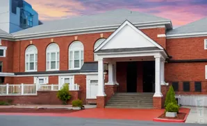 Brick building with arched windows and a covered entrance with stairs.