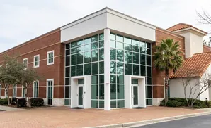 Modern brick building with large glass windows and tiled roof, a palm tree and bare trees outside.