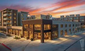 Modern brick and glass building with apartments against a colorful sunset sky.