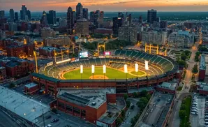 Aerial view of a baseball stadium at dusk, with city skyline and illuminated field.