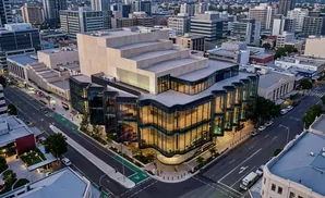 Aerial view of a modern building with curved glass facade and layered geometric upper structure, in a cityscape.